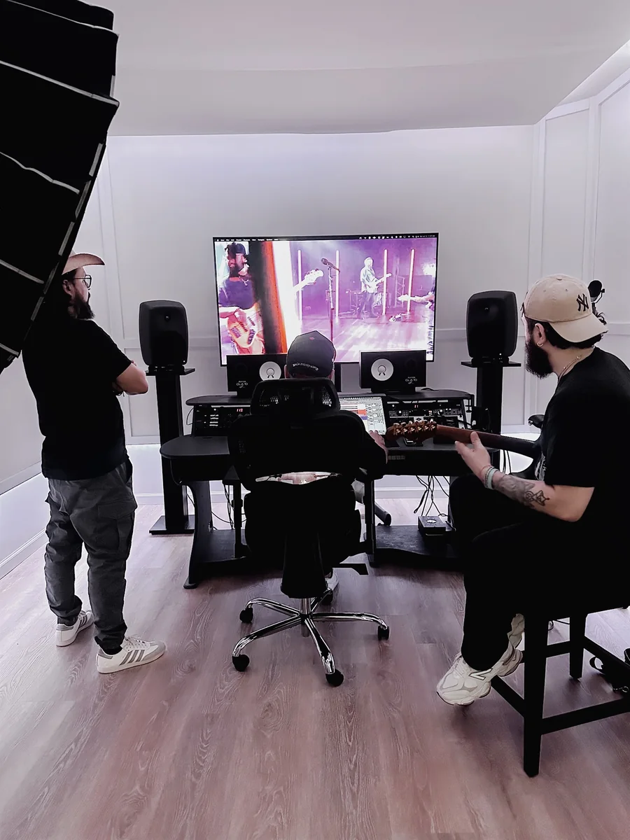 A production session at Nuve — a guitarist on a stool, an engineer at the desk, and a live performance playing back on the wall screen.